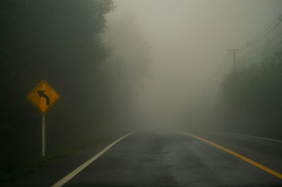 Road sign against trees during foggy weather