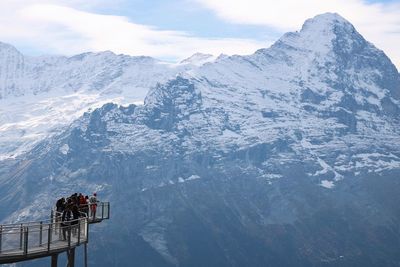 People on observation point against snowcapped mountain and sky