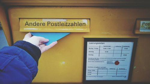 Cropped image of woman putting letter in yellow mailbox