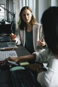Businesswoman gesturing while explaining female colleague at desk in office