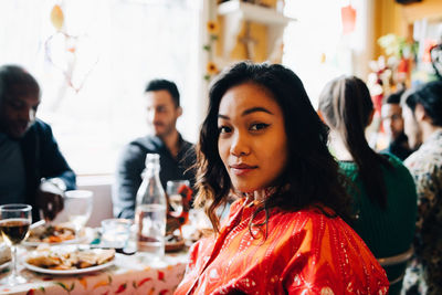 Portrait of confident young woman sitting at table against multi-ethnic friends enjoying brunch in restaurant