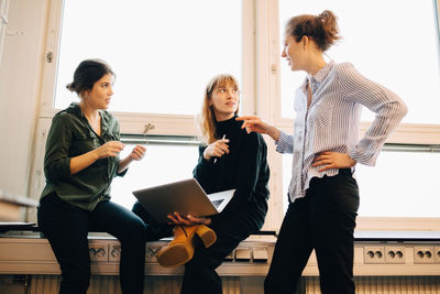 Low angle view of confident female colleagues discussing against window at creative office
