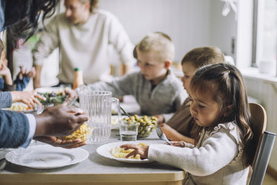 Teacher serving food to male and female students for breakfast in day care center