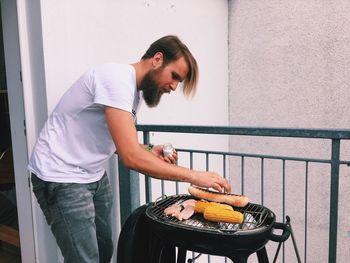 Young man cooking food on barbecue grill at balcony