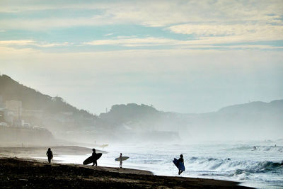 Silhouette people on beach against sky during foggy morning