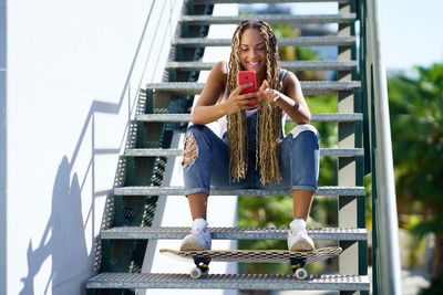Woman with braided hair using smart phone sitting on steps