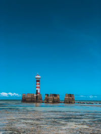 Lighthouse by sea against clear blue sky