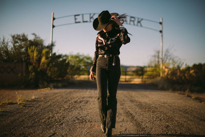 Woman in western wear and cowboy hat walking away from a ranch