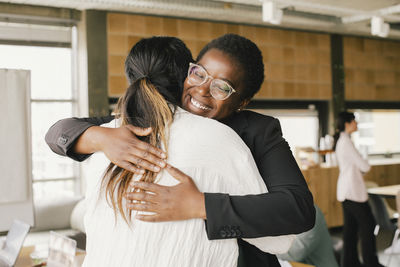 Happy businesswoman embracing non-binary colleague at office