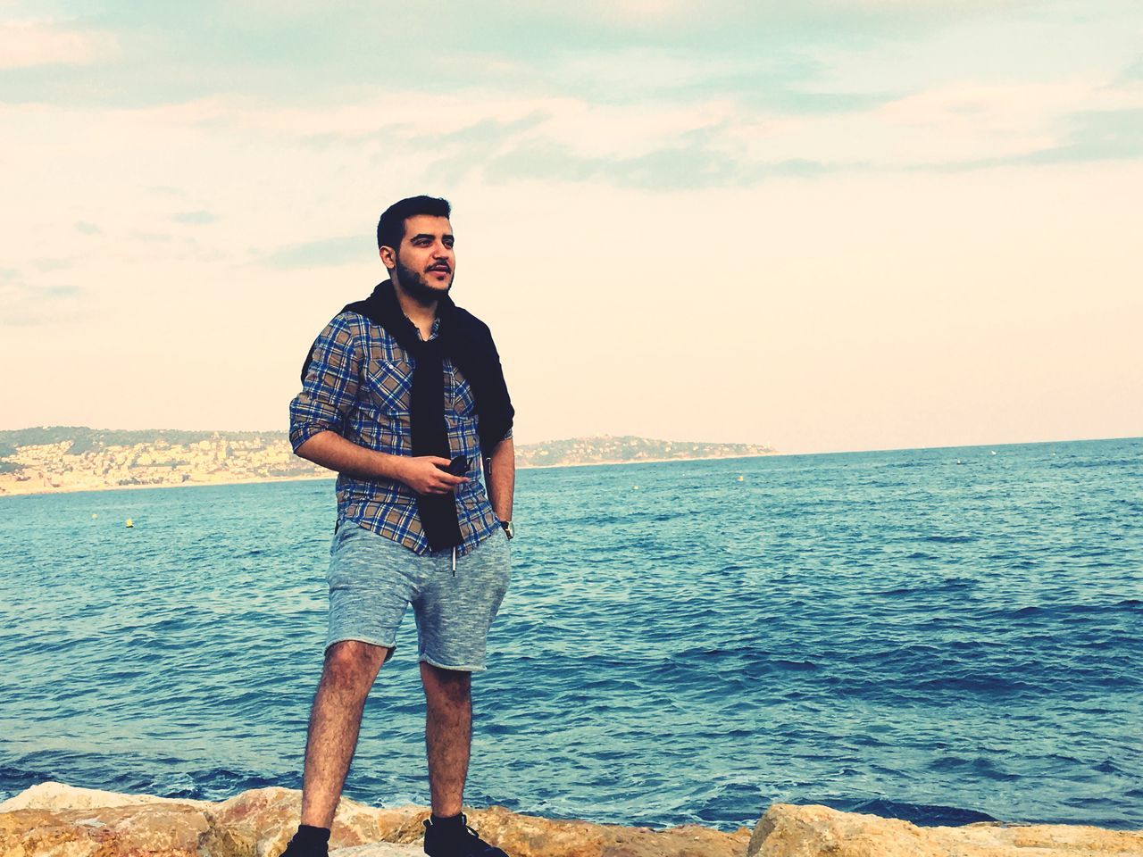 sea, horizon over water, standing, real people, water, one person, nature, sky, casual clothing, looking at camera, front view, leisure activity, outdoors, scenics, portrait, lifestyles, beauty in nature, tranquil scene, young men, full length, young adult, cloud - sky, smiling, day