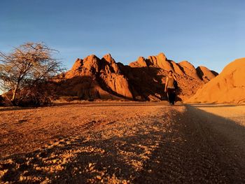 Man walking at desert with mountains in background against blue sky during sunset