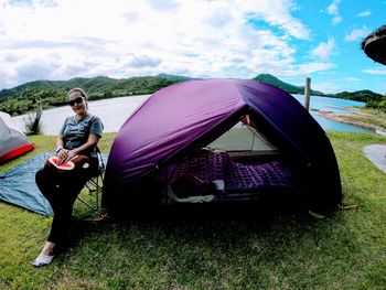 Side view of man sitting at tent against sky