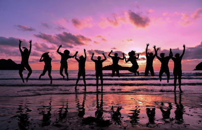 Silhouette people jumping at beach against sky during sunset