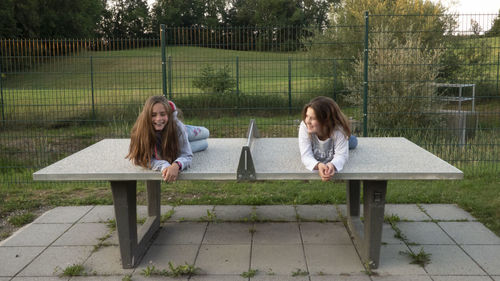 Two women sitting on bench against plants