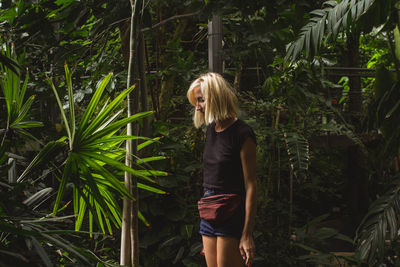 Young woman standing by trees in forest