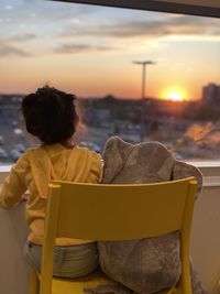 A child watching the sunset next to her doll