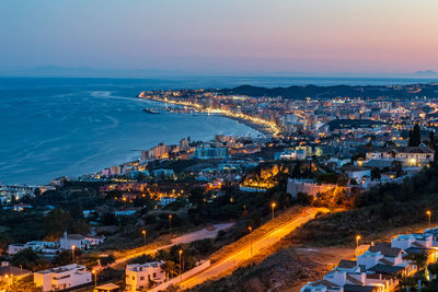 High angle view of illuminated city by sea against sky