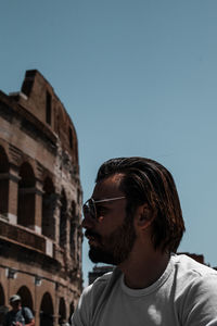 Side view of young man looking away against clear blue sky