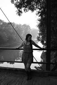 Full length of young woman standing on bridge over river