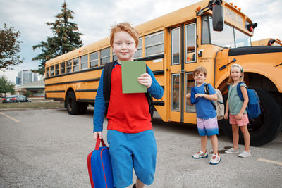 Happy caucasian children boys and girl kids students standing by yellow school bus. education 