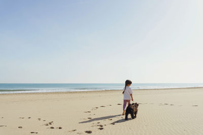 Rear view of woman walking at beach against clear sky