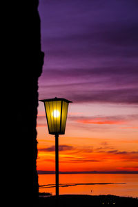 Illuminated gas light against dramatic sky during sunset