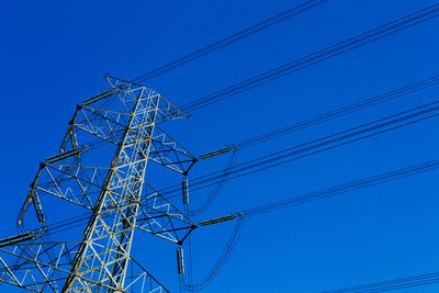 Low angle view of electricity pylon against blue sky