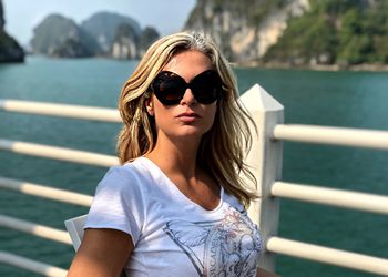 Young woman wearing sunglasses on railing against sea