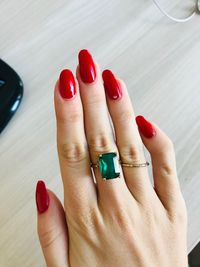 Cropped hand of woman wearing emerald ring with red nail polish on table