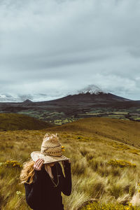 Young woman wearing hat standing on grassy field against cloudy sky