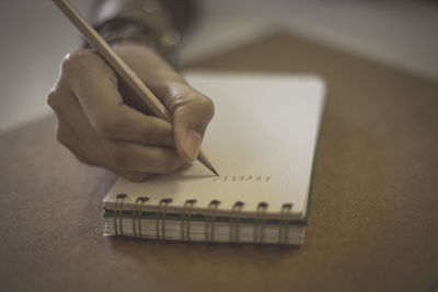 Cropped hand of female student writing on notepad on desk