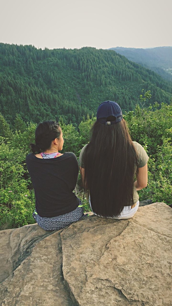 rear view, two people, real people, sitting, lifestyles, nature, leisure activity, togetherness, day, casual clothing, women, tree, landscape, mountain, outdoors, men, beauty in nature, scenics, clear sky, bonding, full length, friendship, sky, young adult