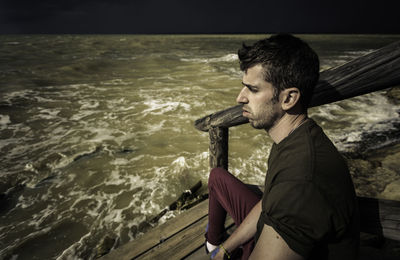 Young man looking away while standing by sea