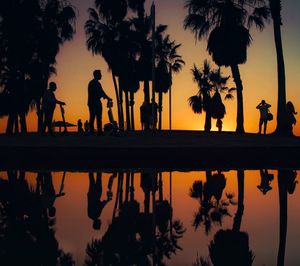 Silhouette people by lake against sky during sunset