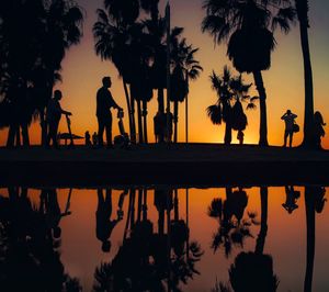 Silhouette people by swimming pool against sky during sunset