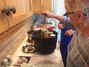 Senior woman removing mason jars from saucepan in kitchen