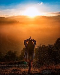 Rear view of woman practicing yoga while standing on field against sky during sunset