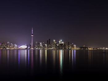 Illuminated cn tower and cityscape by river at night