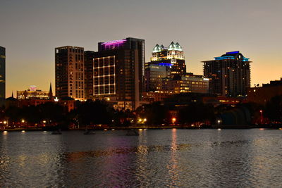 Illuminated buildings by river against sky in city at night