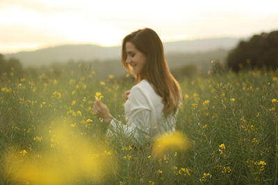 Side view of young woman standing amidst yellow flowers
