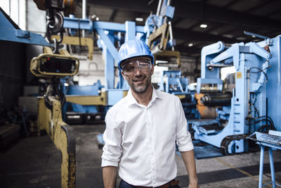 Smiling businessman wearing protective eyewear while standing in industry
