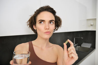 Portrait of young woman drinking glass at home