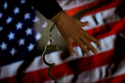 Cropped hand of male criminal with handcuffs against american flag