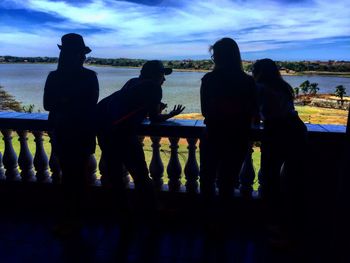 Silhouette people standing by railing against sky during sunset