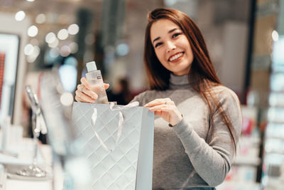 Portrait of smiling young woman holding camera while standing outdoors