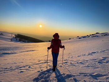 Rear view of woman with hooded winter coat and backpack hiking in the mountains at sunset