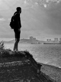 Full length of man standing by sea against sky in city