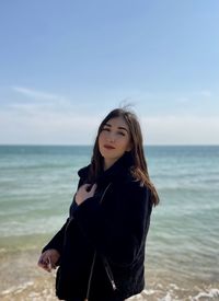 Young woman standing at beach against sky