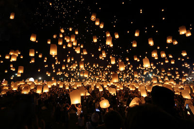 People with illuminated lanterns against sky at night