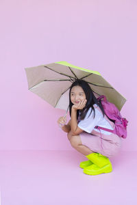 Young woman holding umbrella against pink background